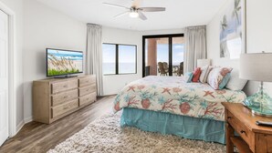 A bedroom with a bed, a TV, a ceiling fan, a window, and a door leading to a balcony. - Four Seasons 502-e Fishing Pier Newly Remodeled 3 Bedrooms (Orange Beach)