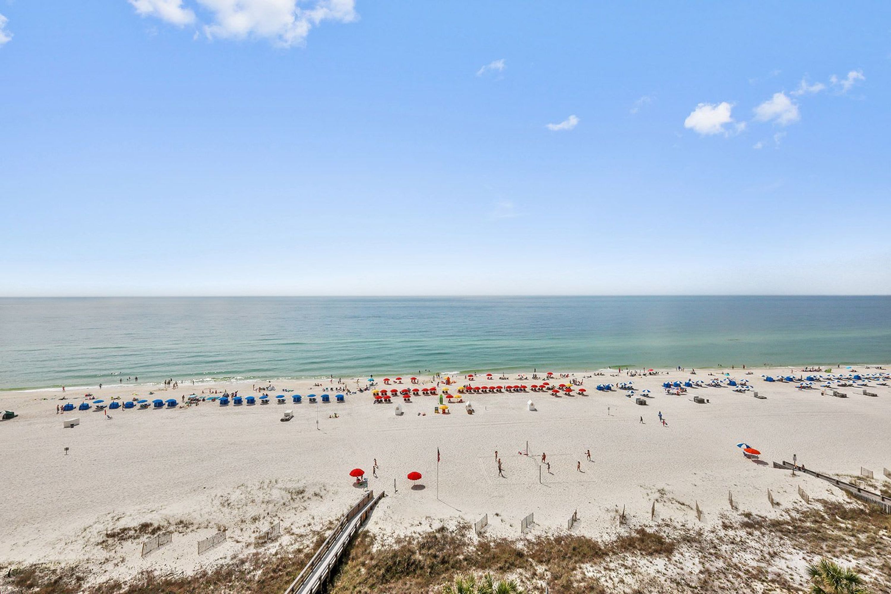 Une plage dotée de nombreux parasols et de chaises longues, d’une promenade en bois et offrant une vue dégagée sur l’océan.