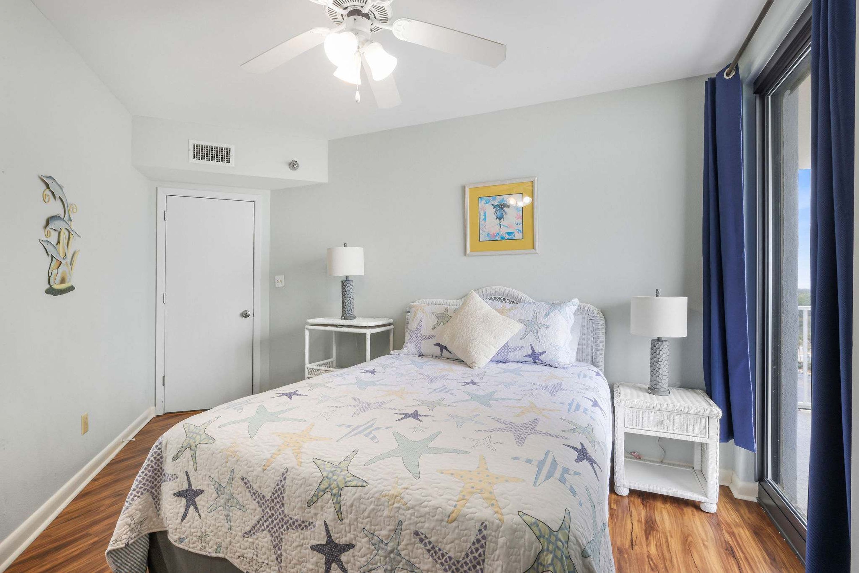 A bedroom with a bed, nightstands, a ceiling fan, a window with curtains, and a wall-mounted picture.