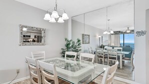 Un comedor con una mesa de vidrio, sillas blancas y una araña.