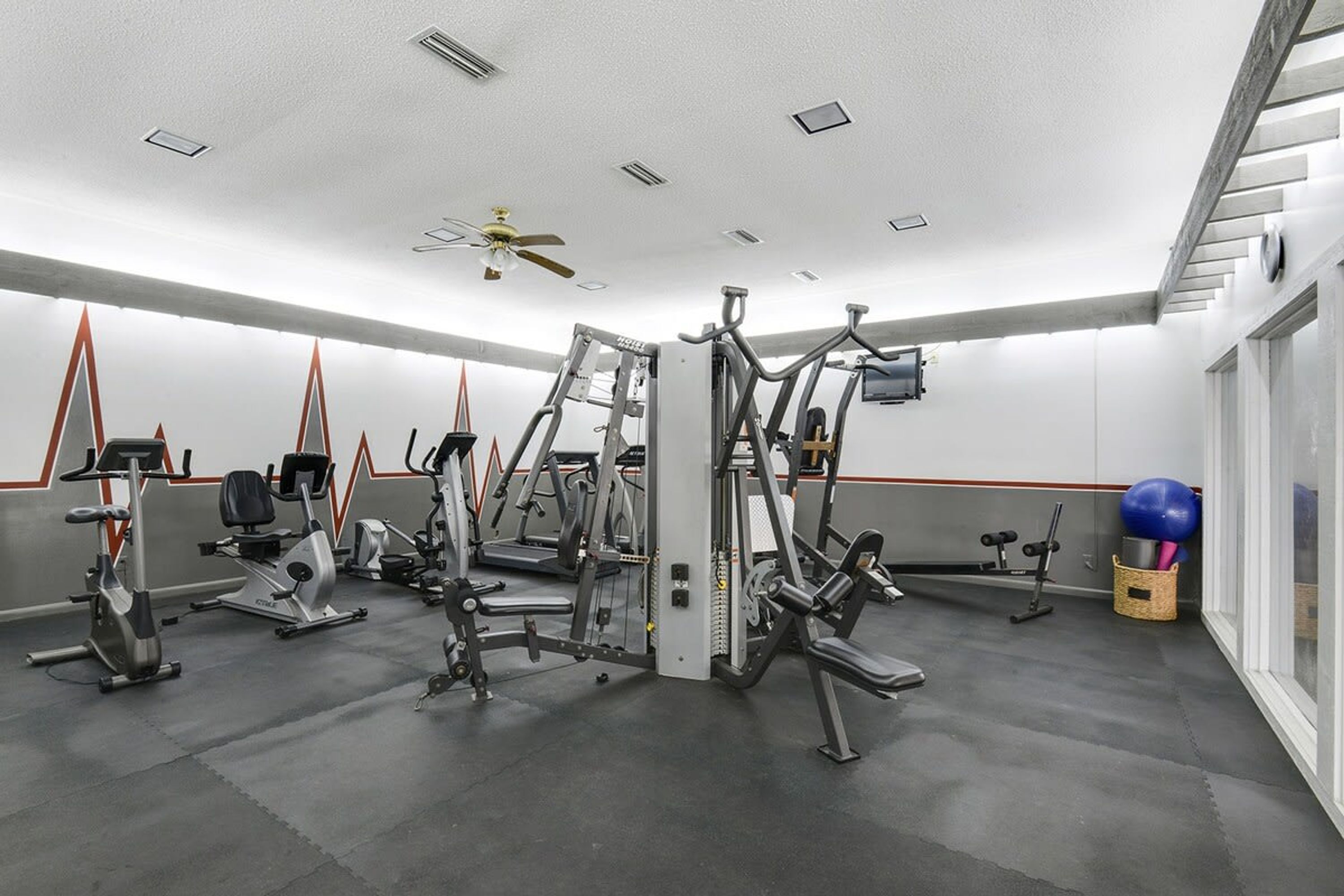 Ein Fitnessstudio mit verschiedenen Trainingsgeräten, darunter Laufbänder, Ergometer und Kraftgeräte.