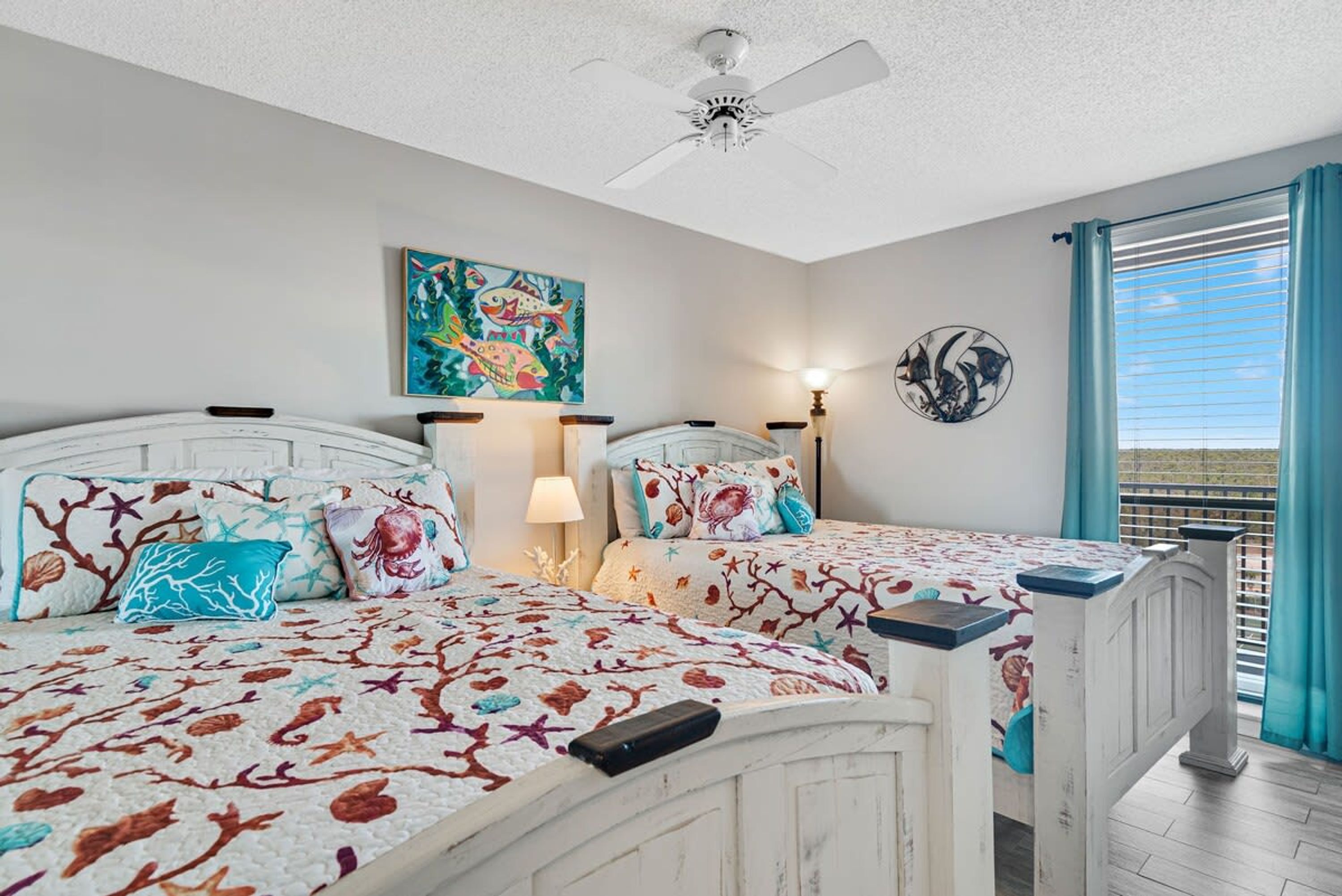 A bedroom with two beds, a ceiling fan, artwork, and a view of the outdoors.