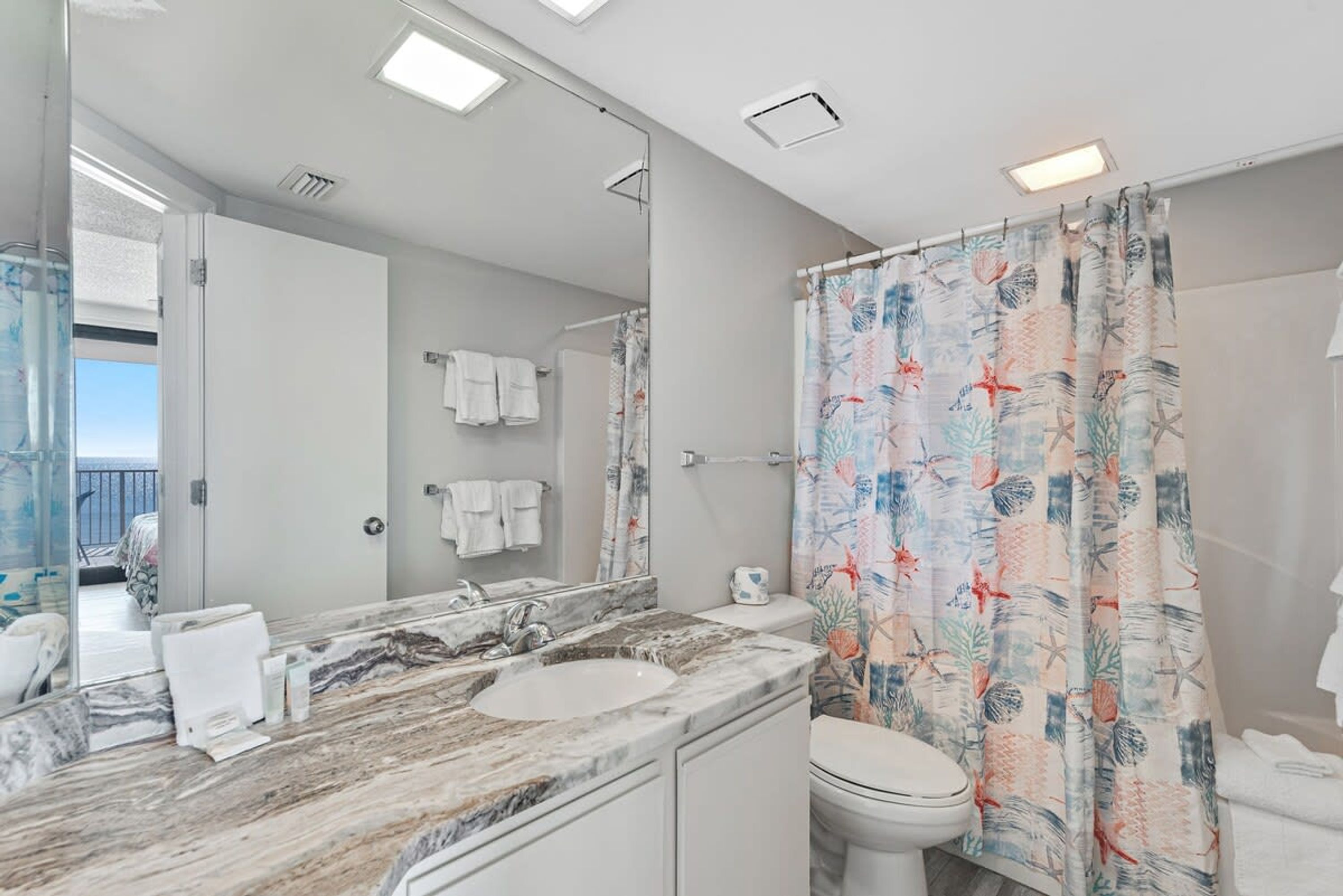 A bathroom with a marble sink, a toilet, and a shower curtain with a tropical print.