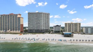 Un hotel frente a la playa con varios edificios altos, una playa arenosa con sombrillas y un muelle.