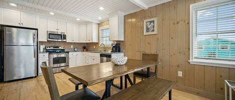 A modern kitchen with wooden walls, white cabinets, stainless steel appliances, and a wooden dining table with benches.