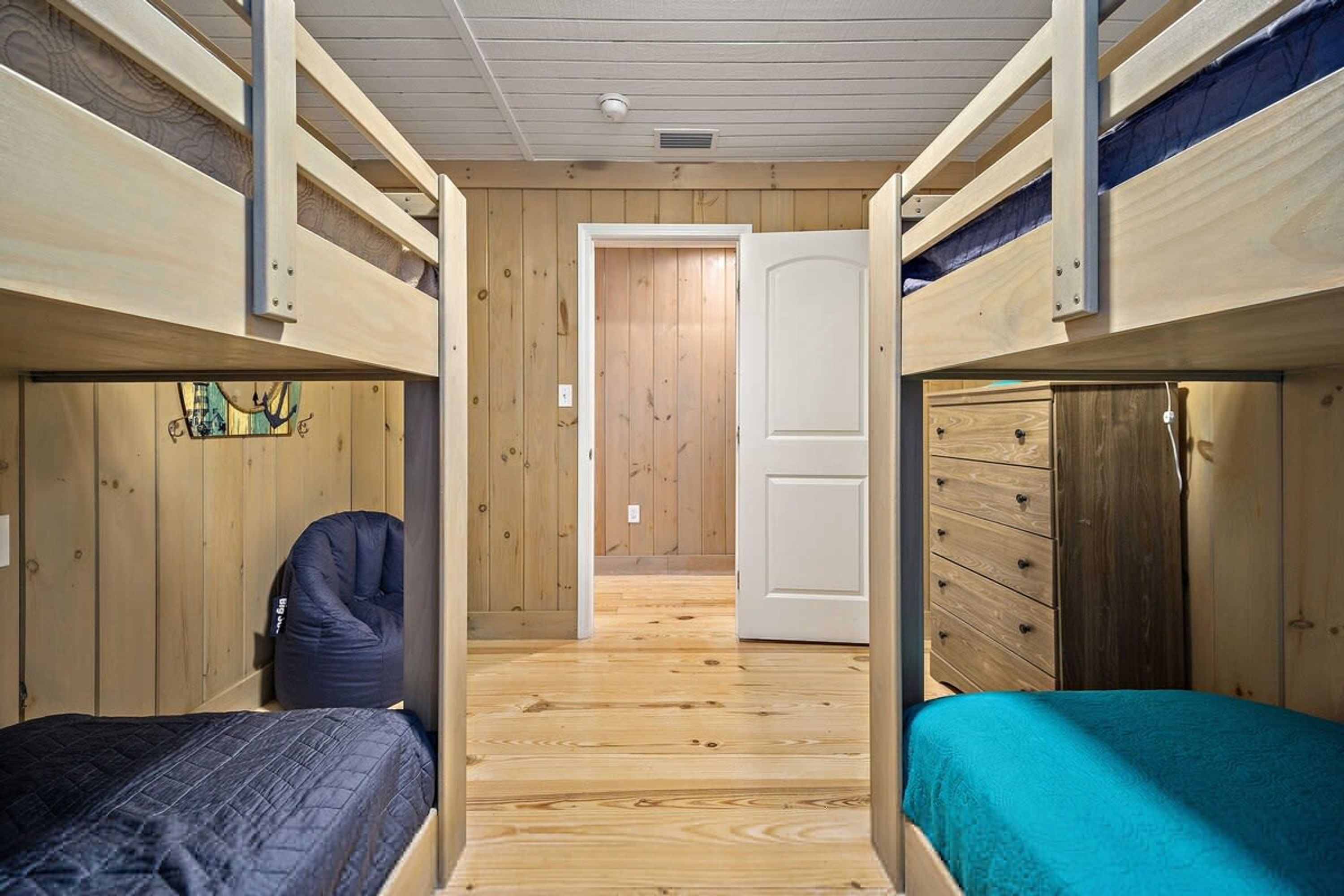 A room with two bunk beds, wooden walls, a door, and a dresser.