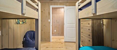 A room with two bunk beds, wooden walls, a door, and a dresser.