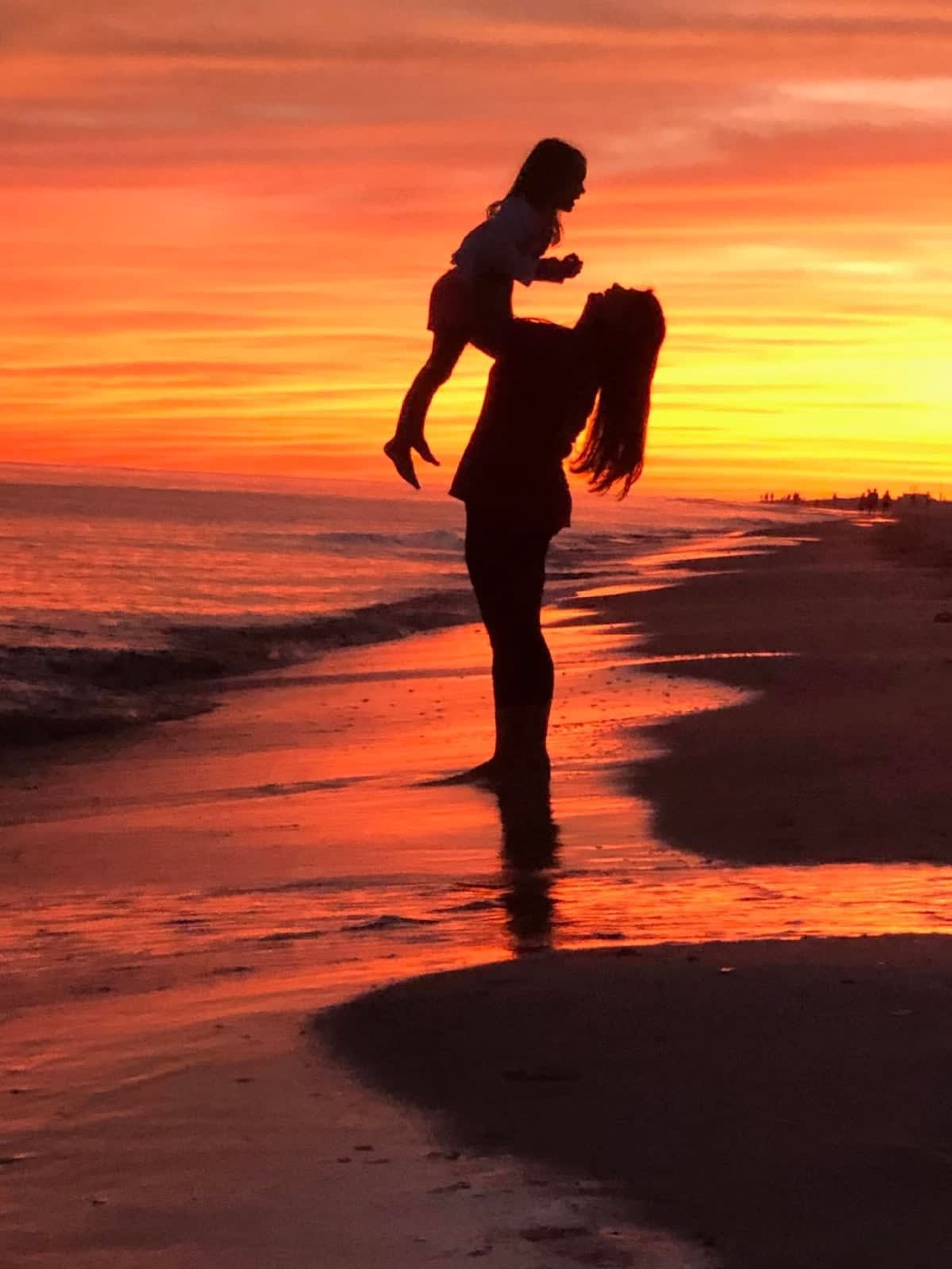 A silhouette of a person carrying a child on a beach at sunset.