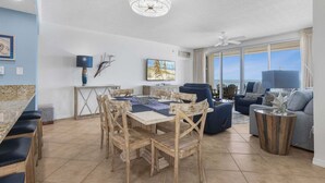 A spacious living area with a dining table, chairs, a sofa, and a TV. - Emerald Key 603 Beachfront Balcony 6th Floor Corner Unit (Orange Beach)