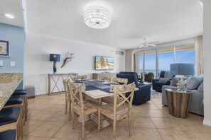 A spacious living area with a dining table, chairs, a sofa, and a TV. - Emerald Key 603 Beachfront Balcony 6th Floor Corner Unit (Orange Beach)
