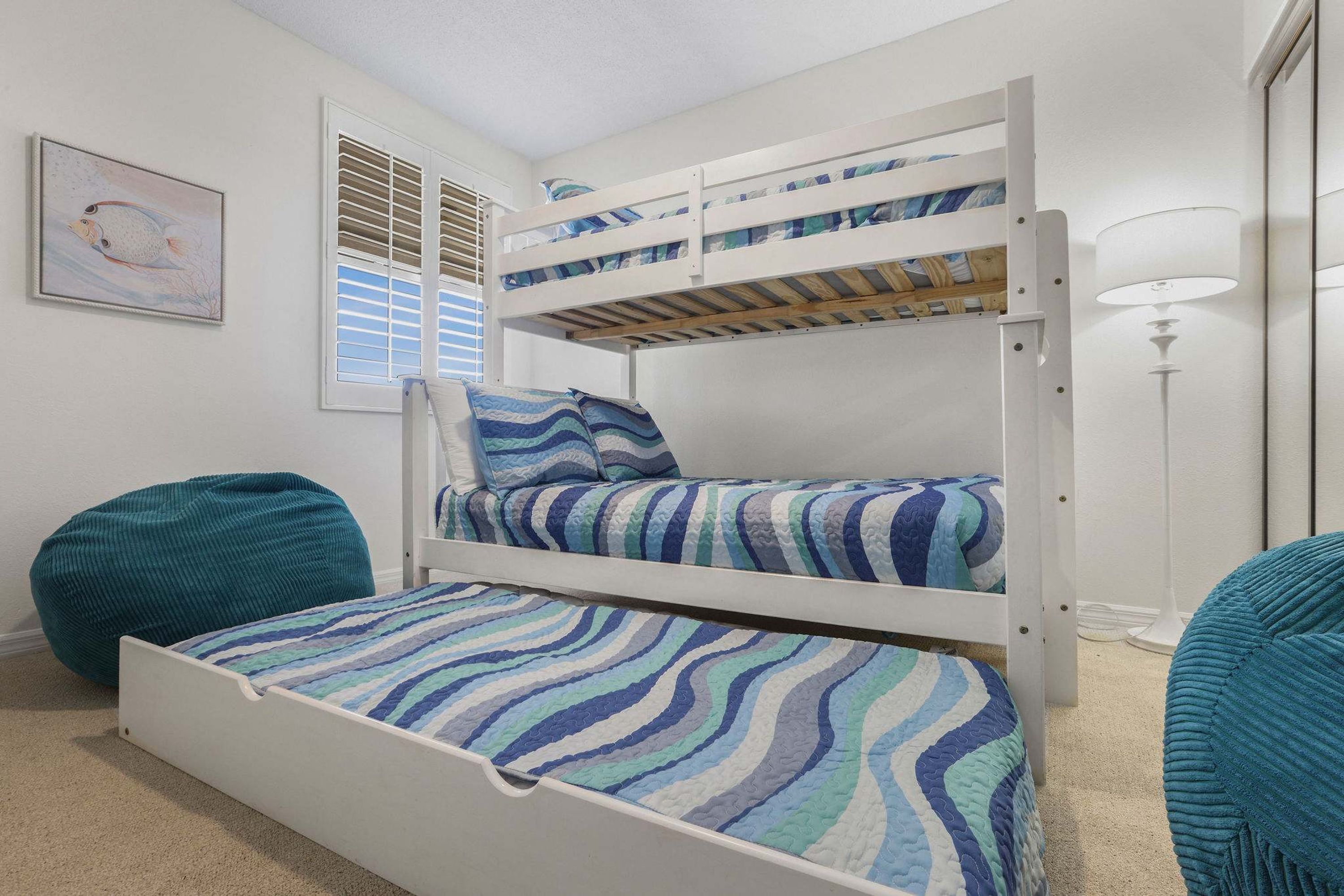 A bunk bed with striped bedding, a bean bag chair, and a wall-mounted lamp.