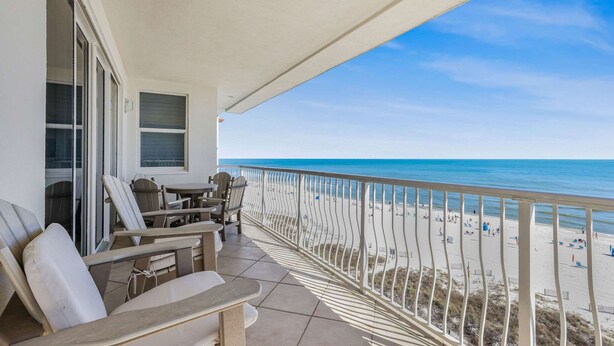 A balcony with a view of the beach, a table with chairs, and a window with blinds. - Emerald Key 603 Beachfront Balcony 6th Floor Corner Unit (Orange Beach)
