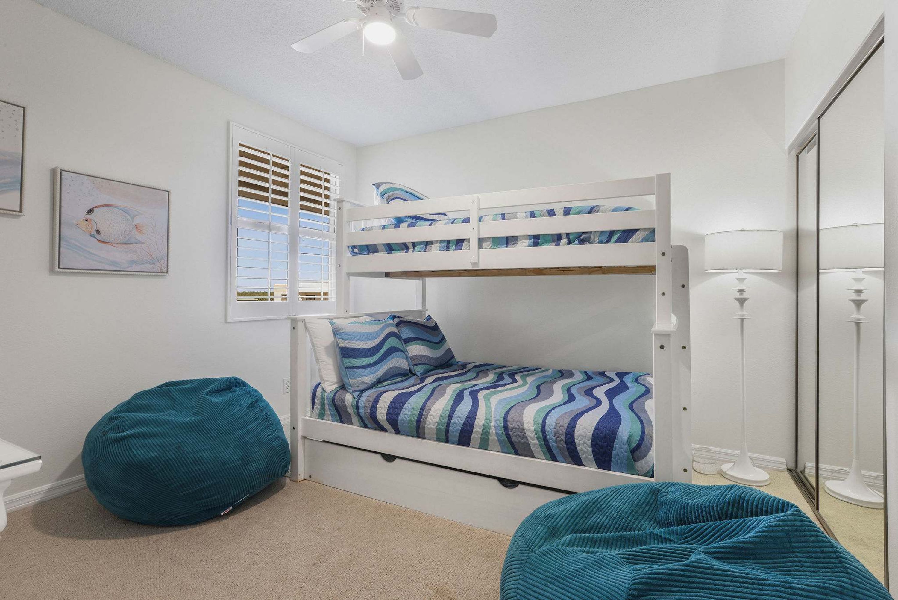 Una cama litera con un edredón a rayas, un sillón de peluche y una lámpara de pie.