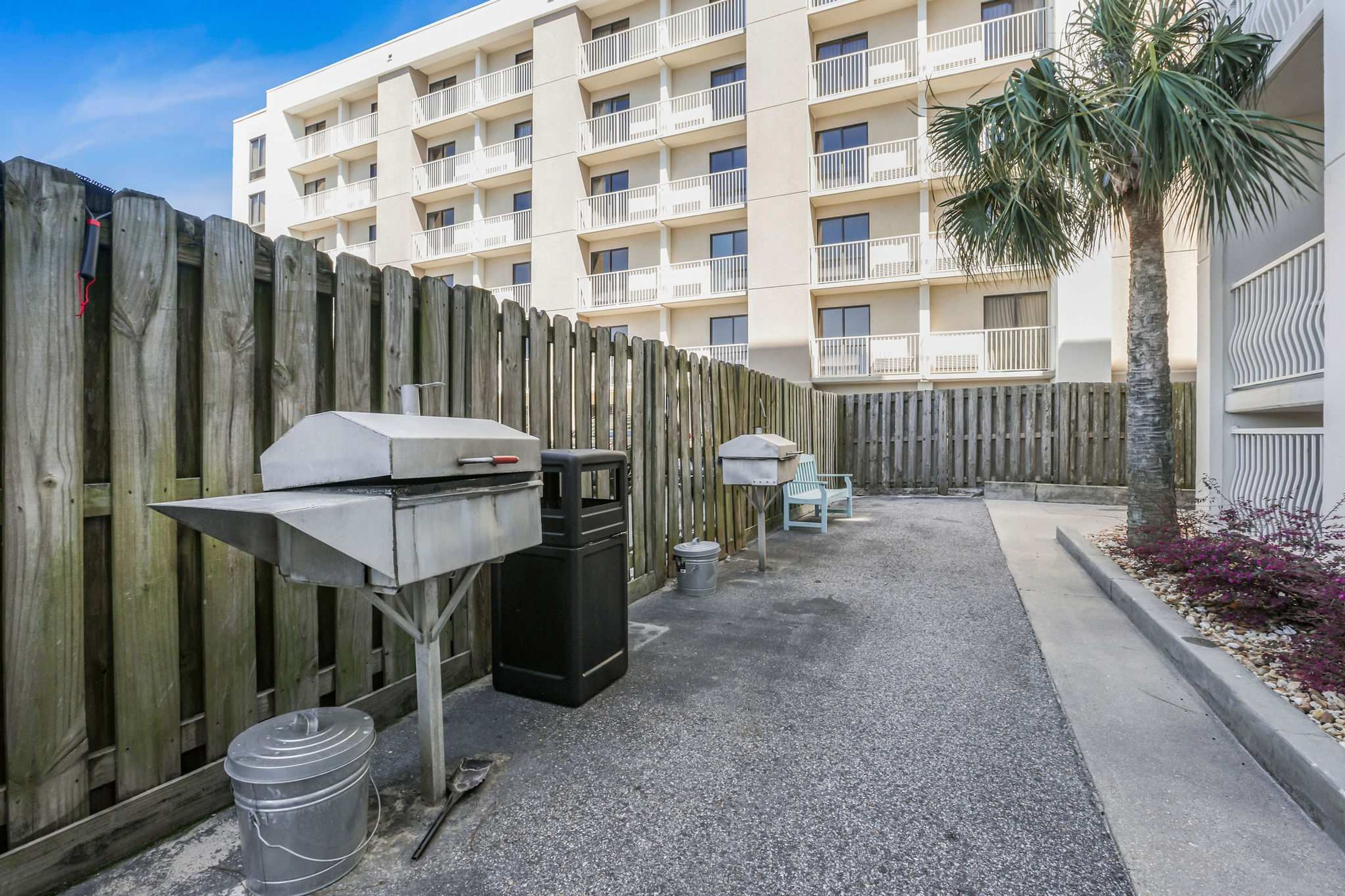 Un espace extérieur aménagé avec un barbecue, des poubelles et une clôture en bois.