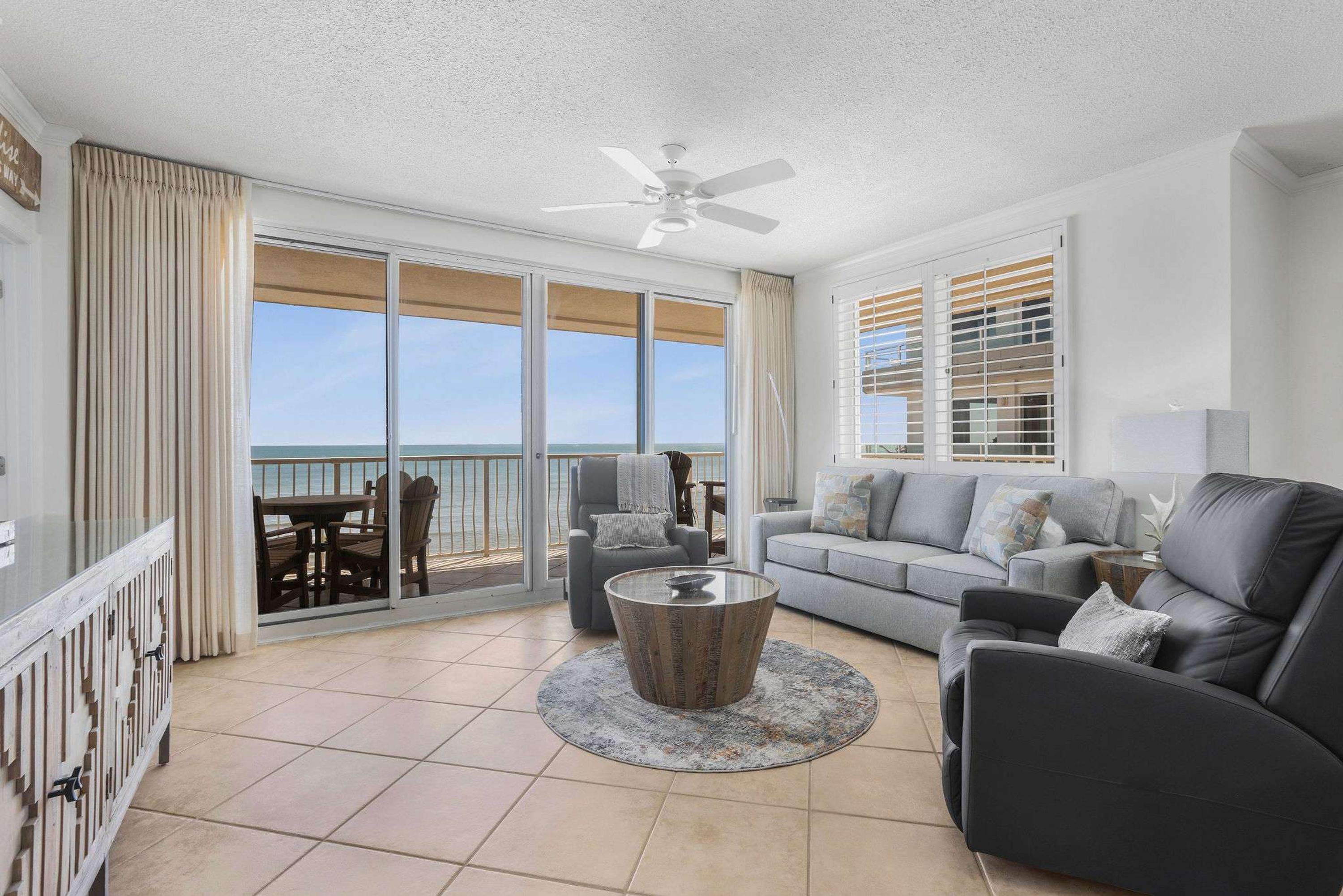 A spacious living room with a balcony, a ceiling fan, and a view of the ocean.