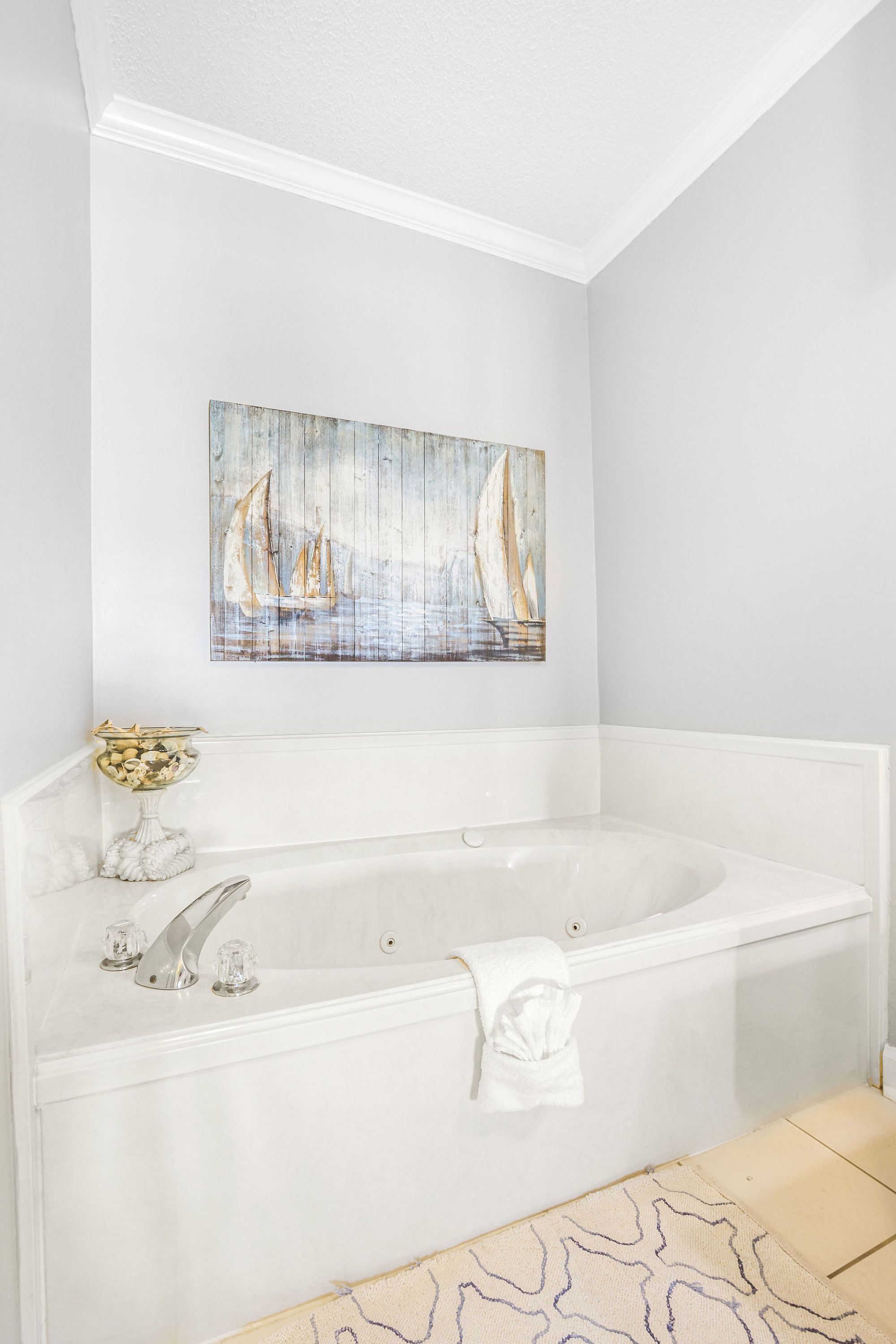A bathroom with a white bathtub, a glass bowl on a pedestal, and a sailboat painting on the wall.