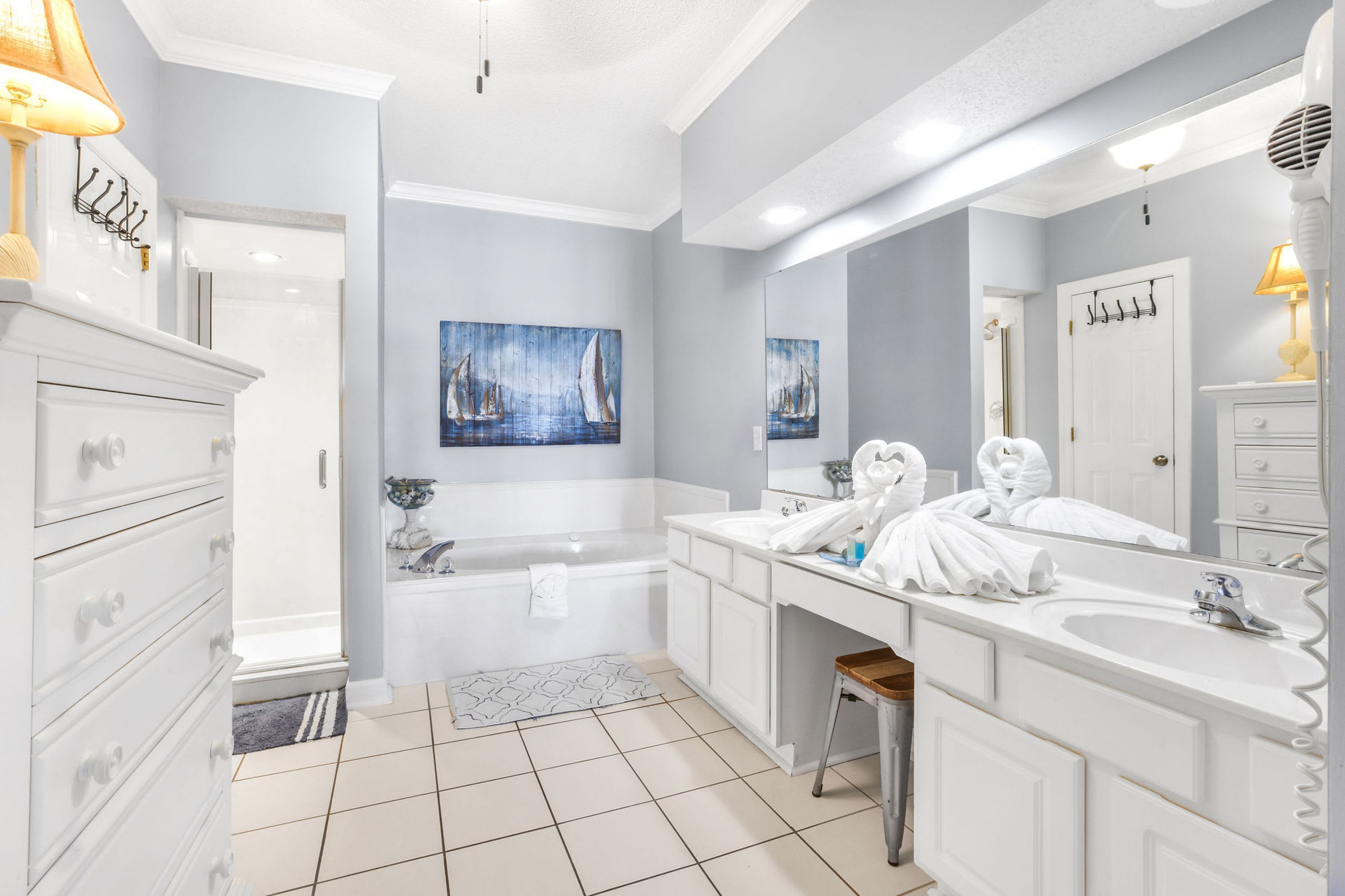 A modern bathroom with a large bathtub, two sinks, and a mirror. There are towels and toiletries on the counter.