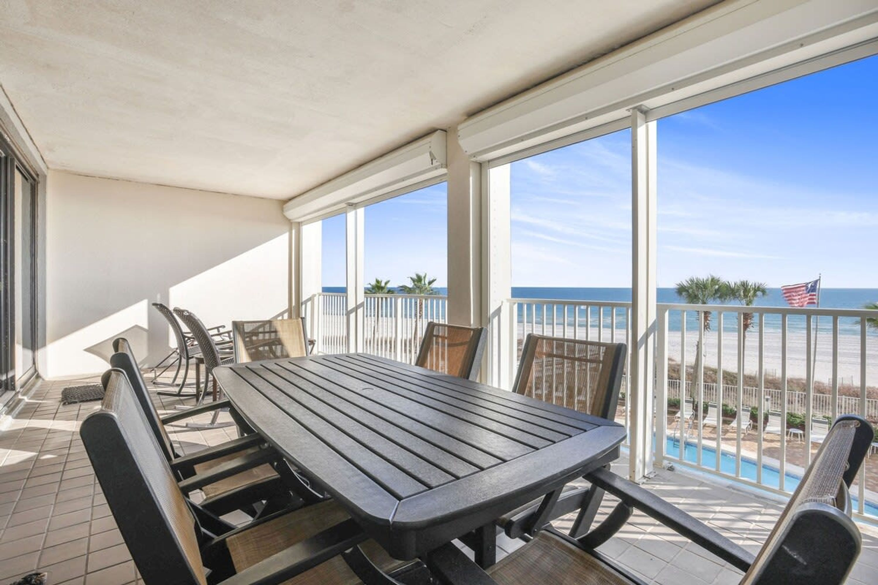 A covered patio with a table and chairs, overlooking a beach with an American flag.