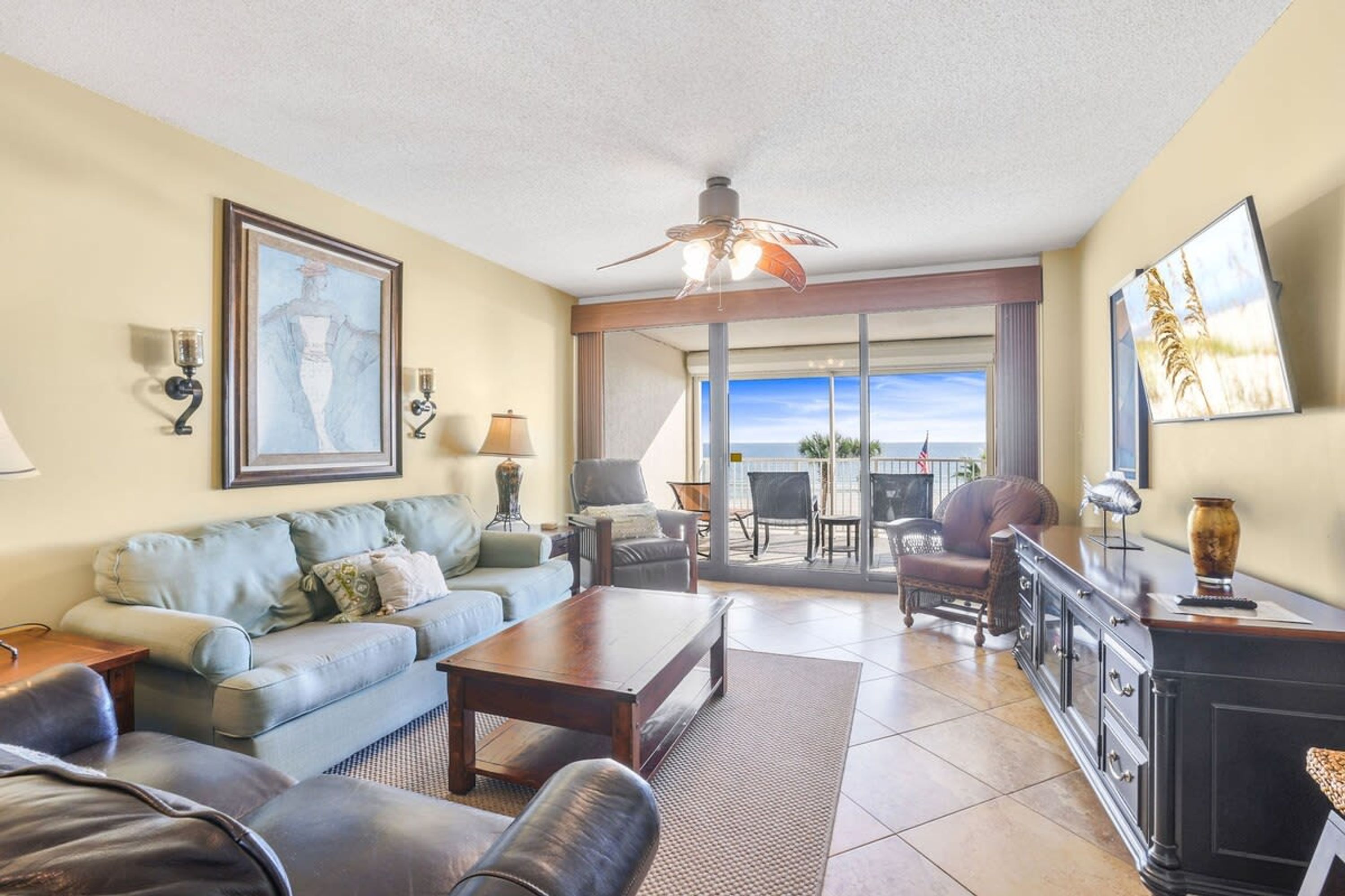 A spacious living room with a sofa, coffee table, and a fireplace. There is a balcony with a view of the ocean.