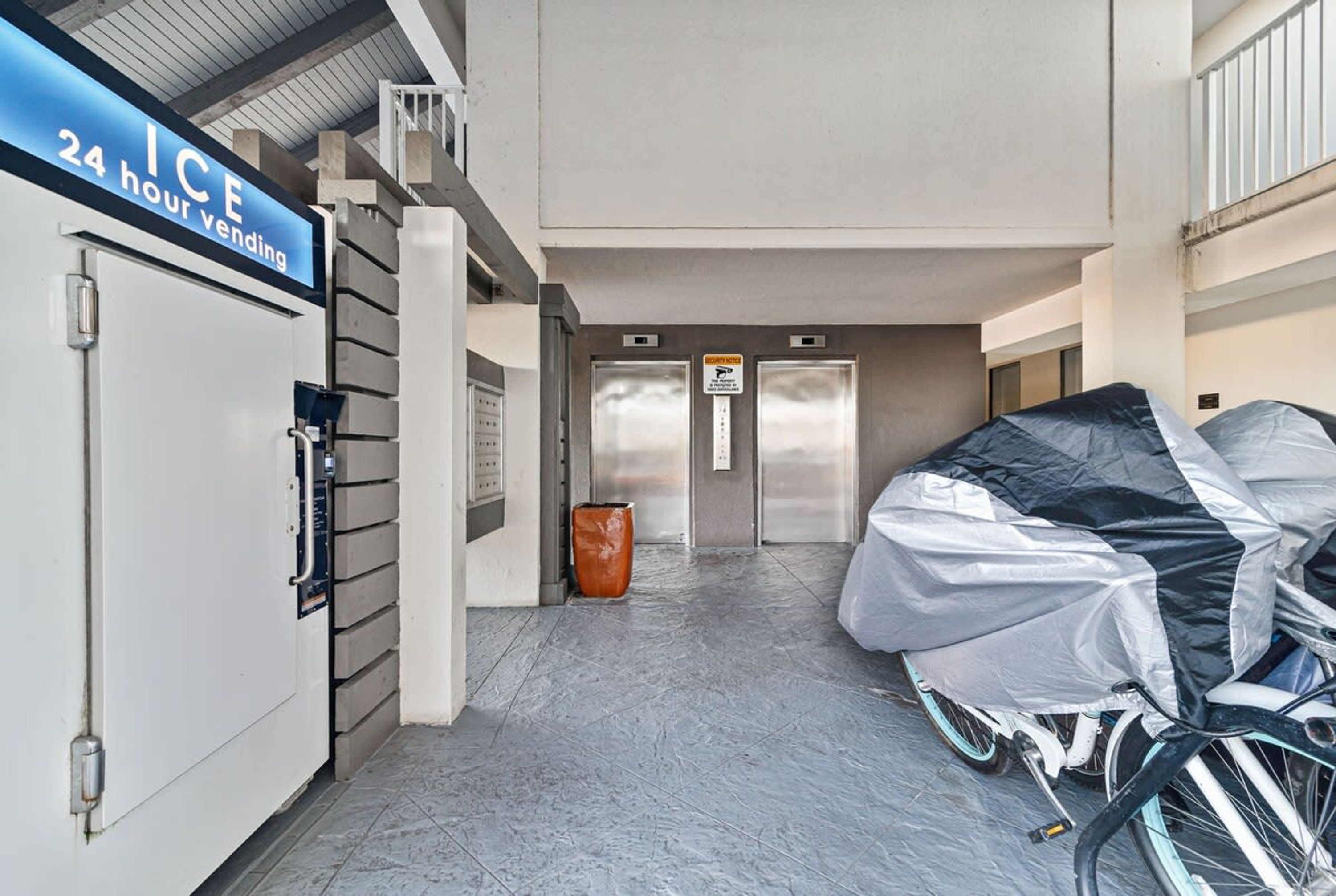 A 24-hour ice vending machine, elevators, and a covered bicycle in a hallway.