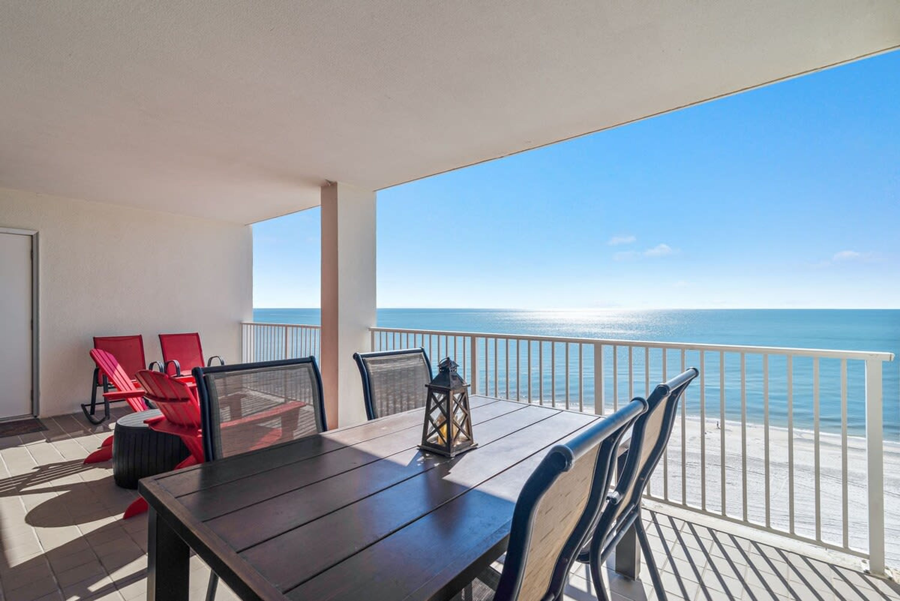 A balcony with a wooden table and chairs, a lantern, and a view of the ocean.