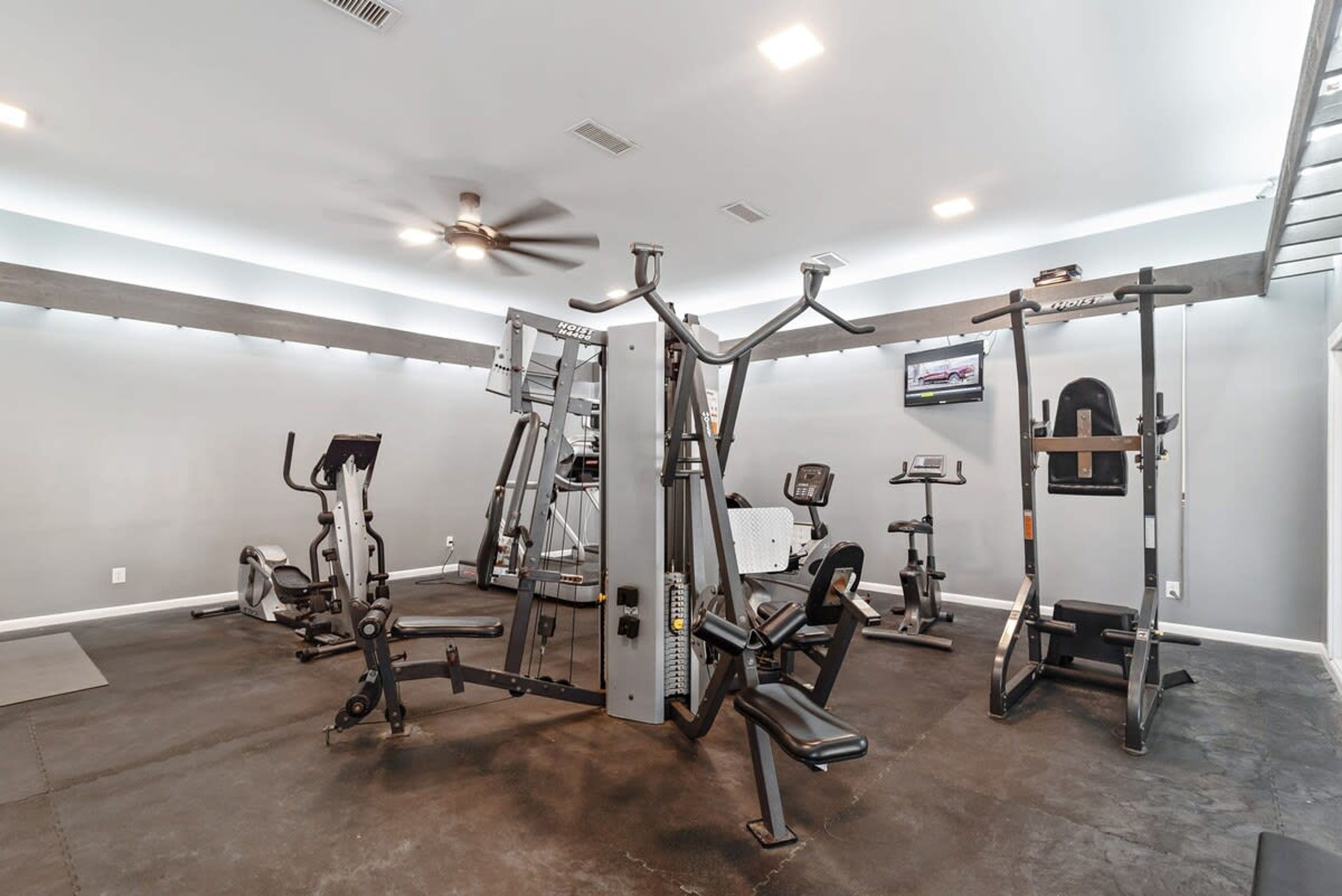 A home gym with various exercise equipment, a ceiling fan, and a television on the wall.