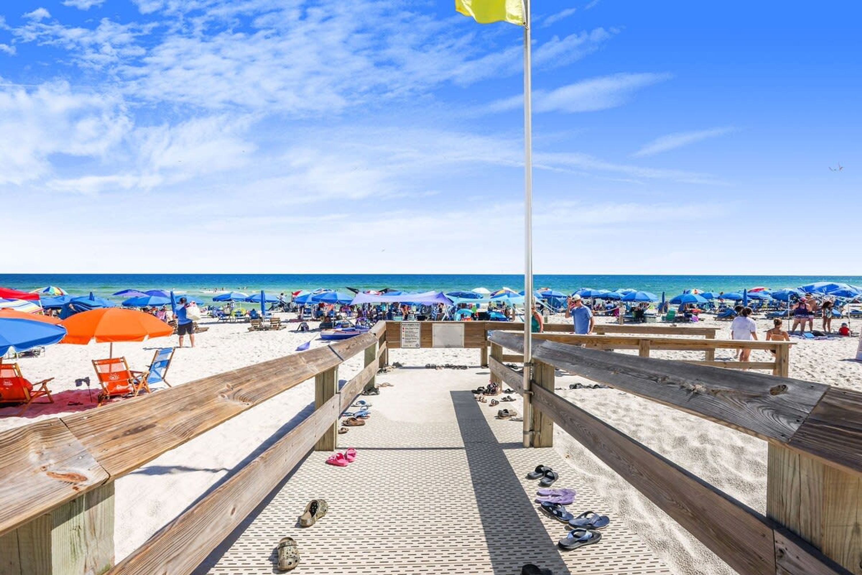A wooden boardwalk leading to a sandy beach with umbrellas and beach chairs.
