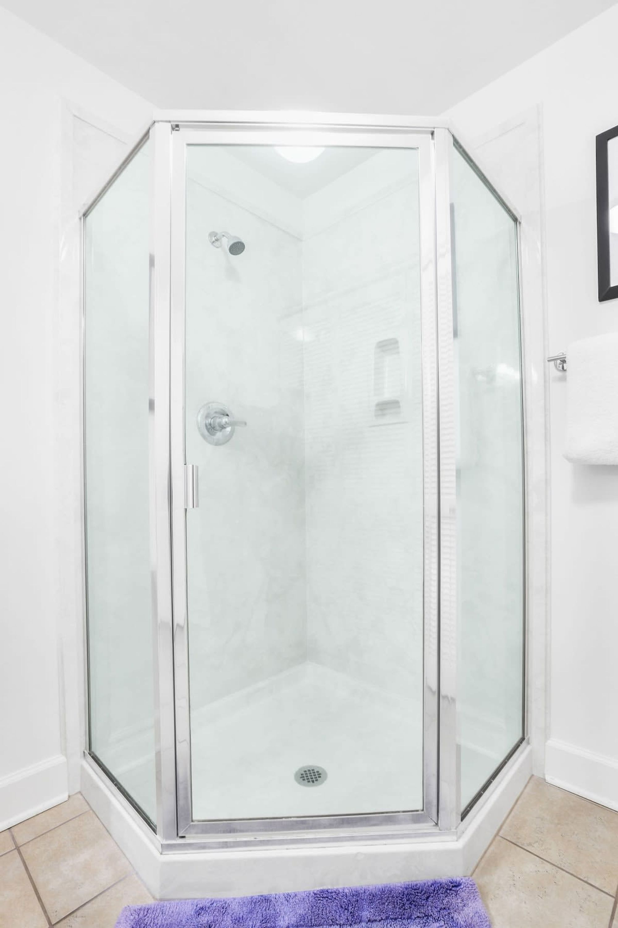 A glass-enclosed shower area with a white tiled floor and a purple bath mat.
