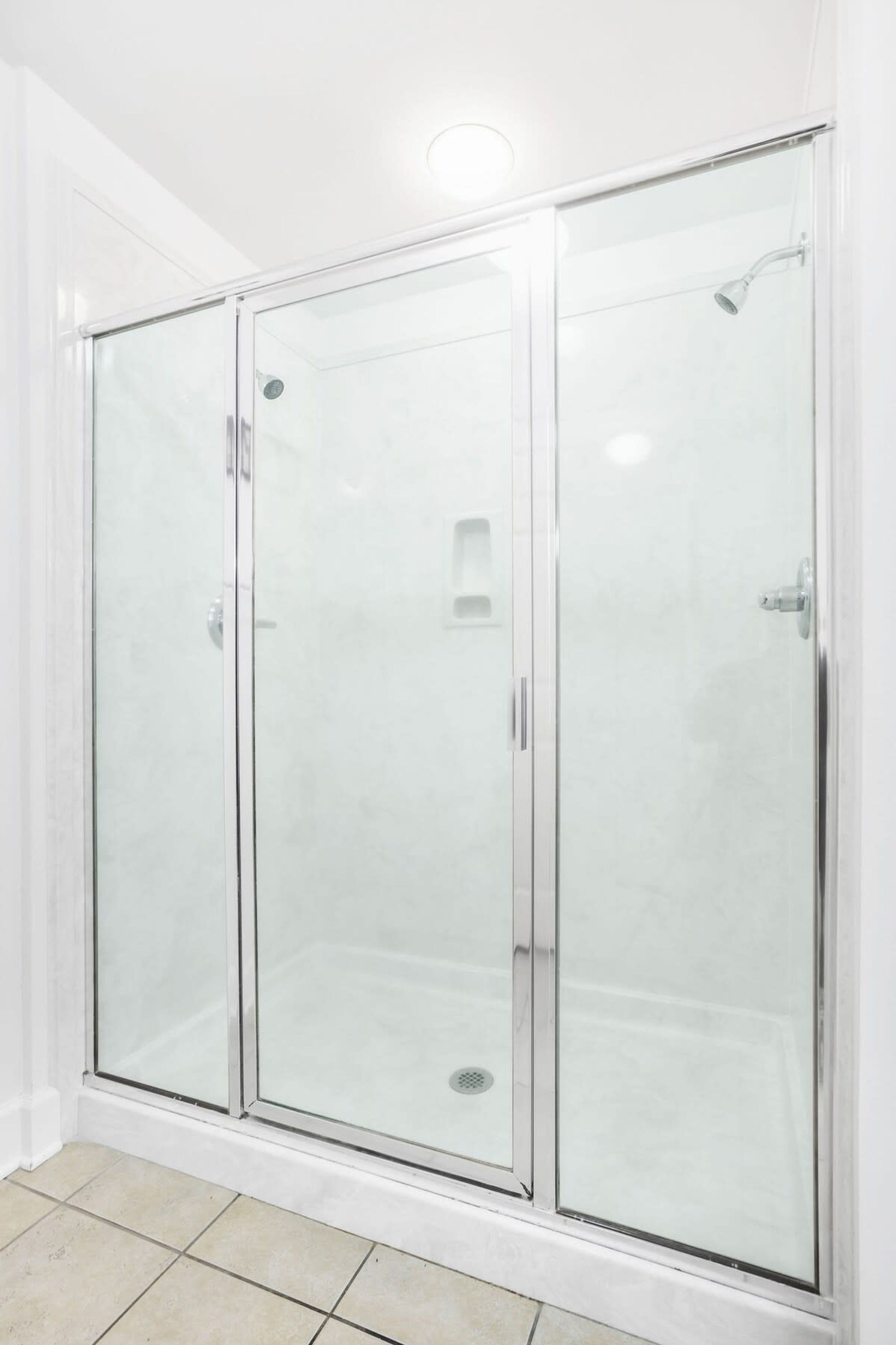 A glass-enclosed shower stall with a white tiled floor and a visible drain.
