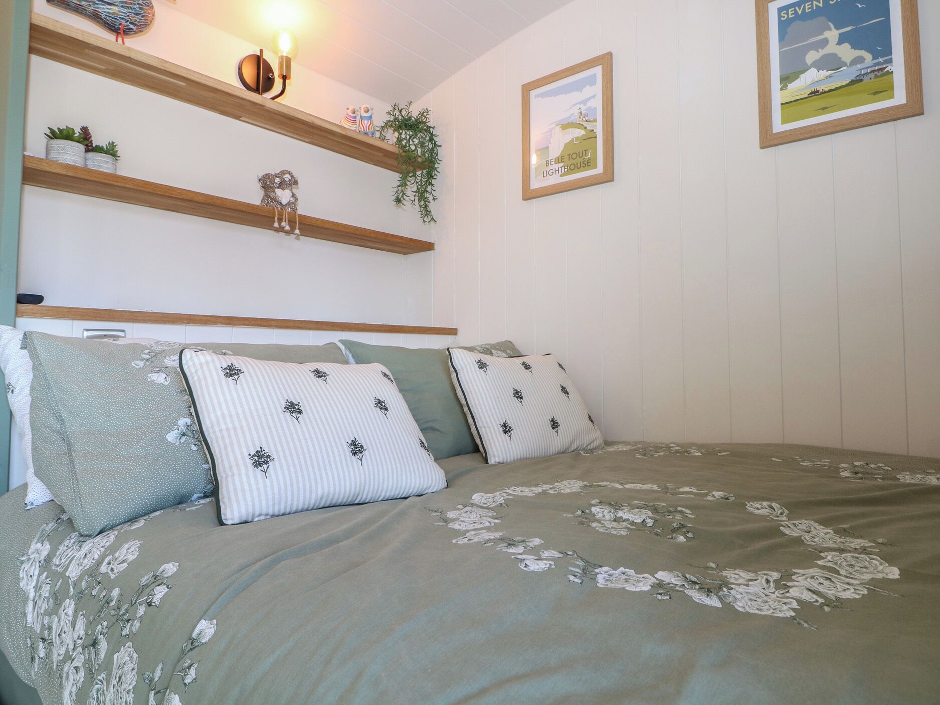 Ein Schlafzimmer mit einem Bett, Kissen, einem Regal mit Dekoration und Wandbildern.