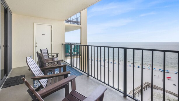 A balcony with a view of the beach, a door, and two wooden chairs. - Phoenix II 2101 3 Bedrooms Amenities Galore Beachfront (Orange Beach)