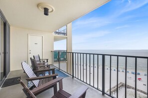Un balcón con vista a la playa, una puerta y dos sillas de madera.