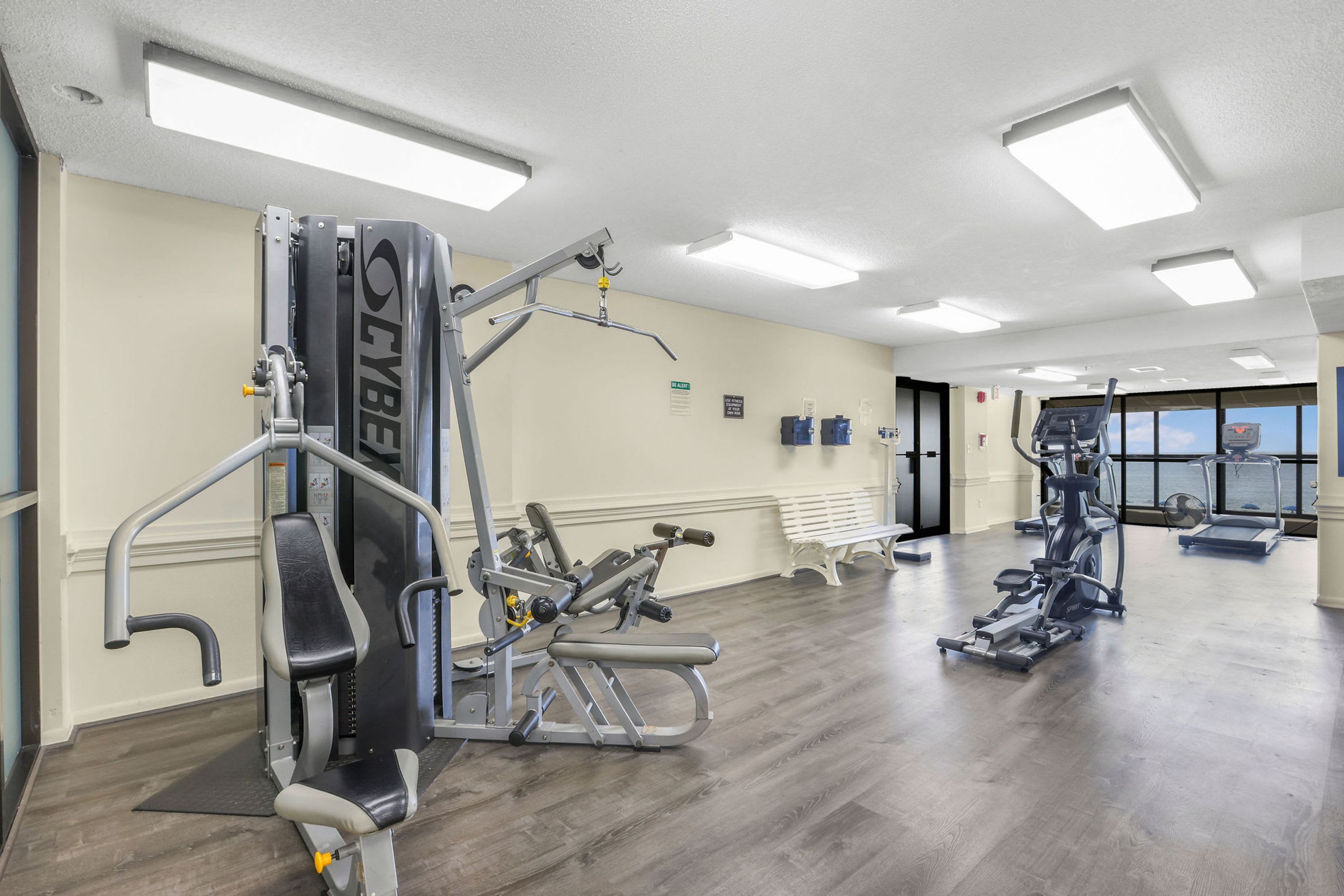 Ein Fitnessraum mit unterschiedlichen Trainingsgeräten, einer Bank und einem Fenster mit Blick ins Freie.