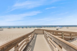 A wooden boardwalk leading to a sandy beach with umbrellas and beachgoers. - Phoenix II 2101 3 Bedrooms Amenities Galore Beachfront (Orange Beach)