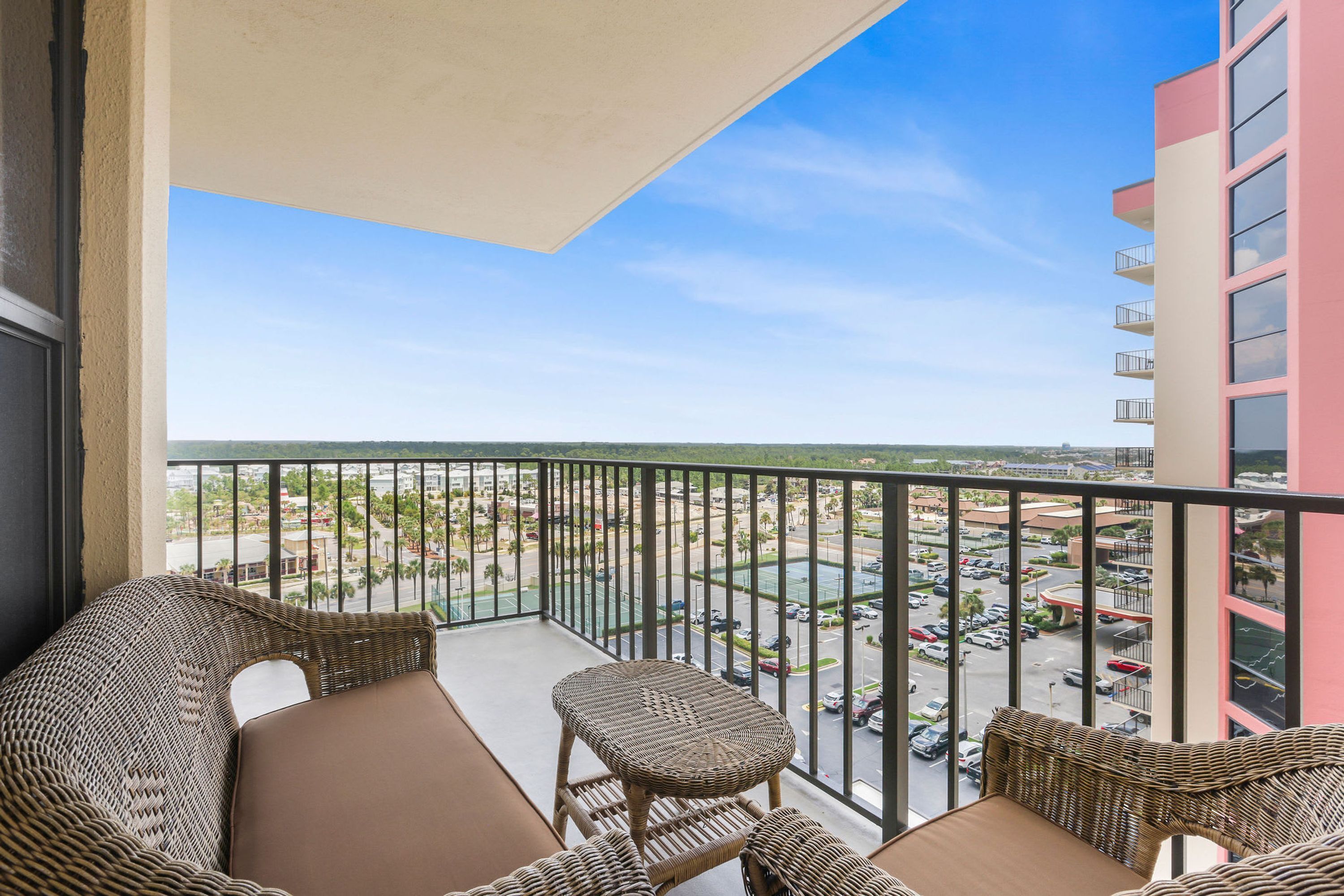 A balcony with wicker furniture and a view of a parking lot and buildings.
