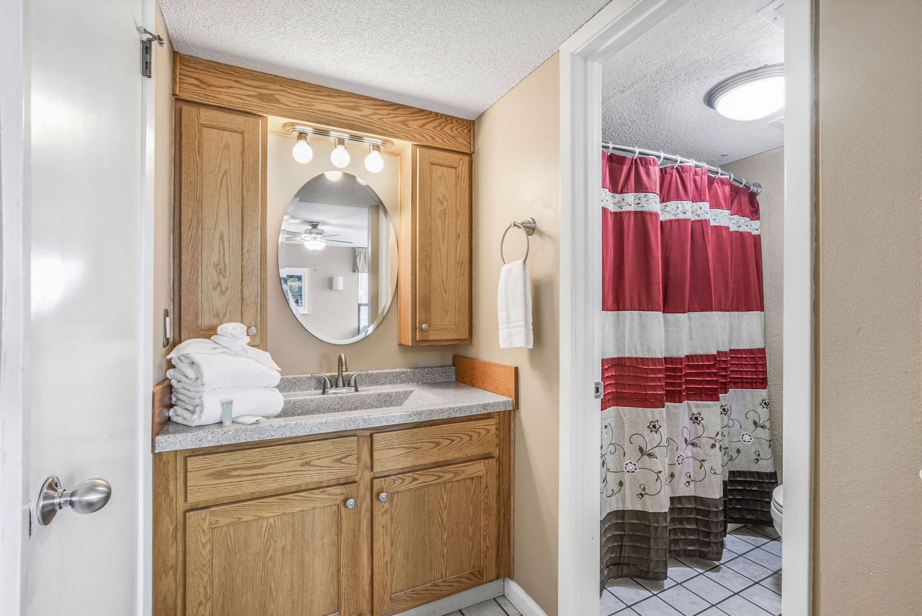 A bathroom with wooden cabinets, a sink, a mirror with lights, and a shower curtain.