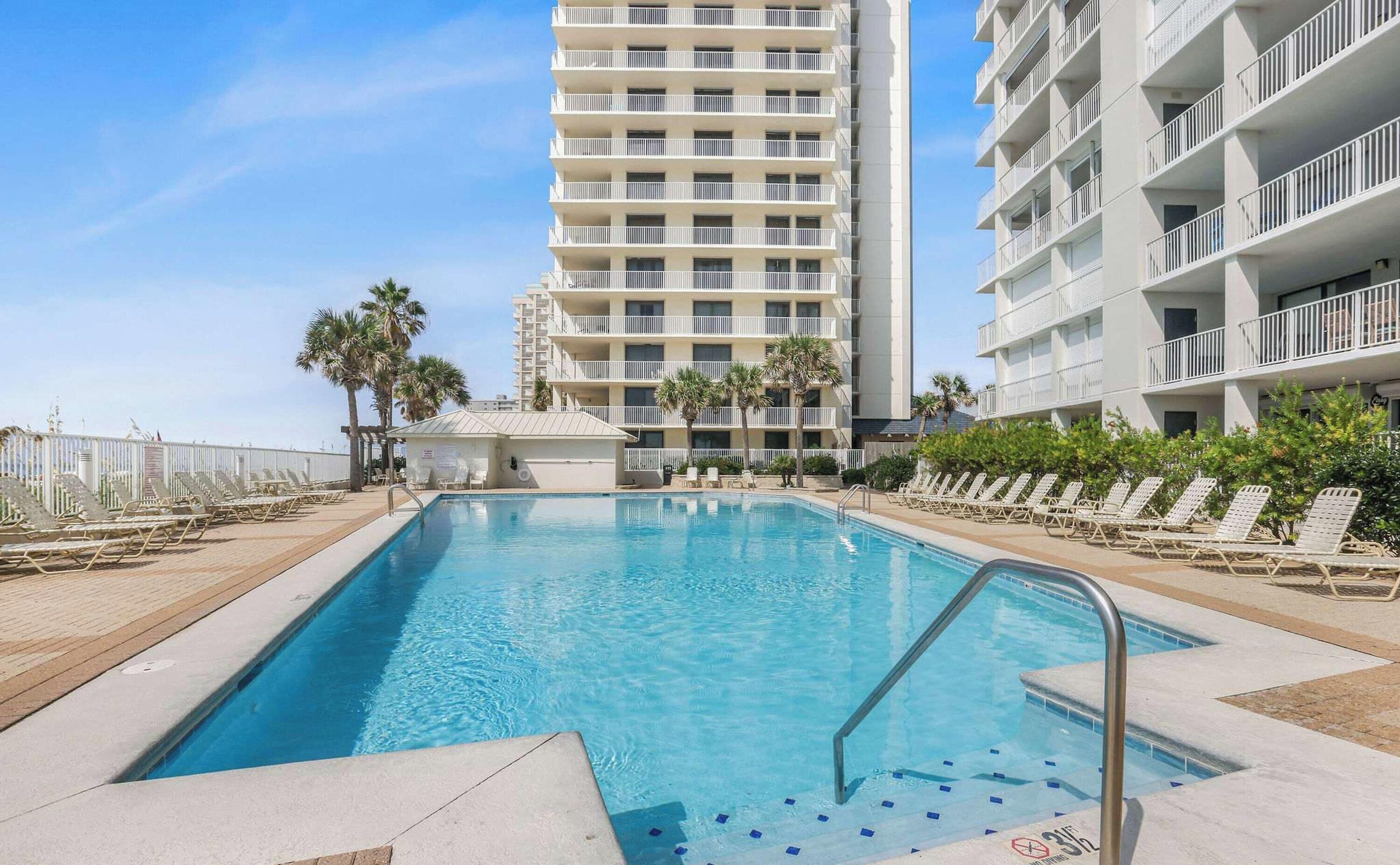 A swimming pool with lounge chairs and palm trees, surrounded by high-rise buildings.