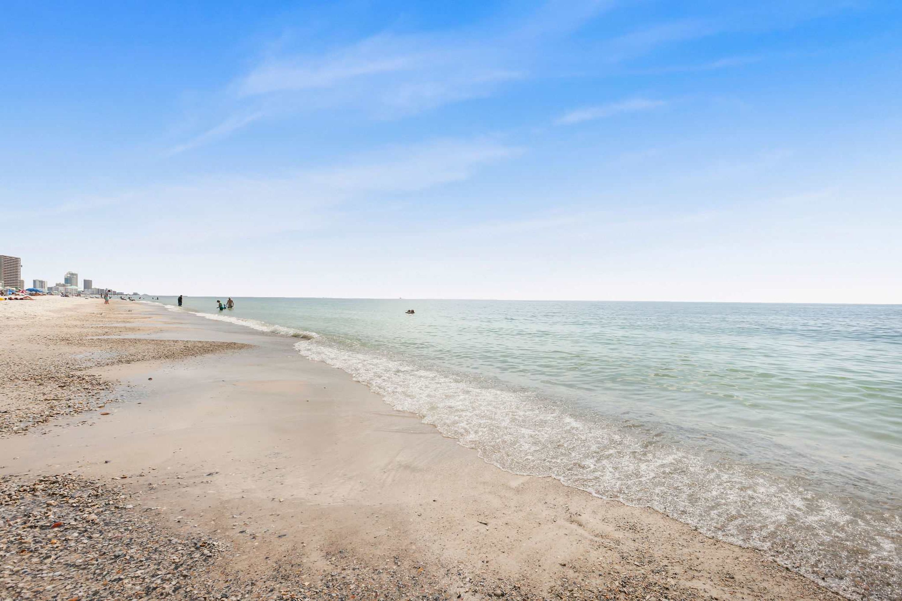 Een strand met kiezels en zand, een heldere lucht en een kalme zee.