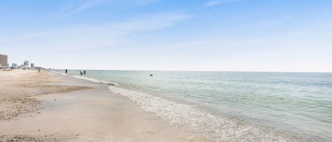 Een strand met kiezels en zand, een heldere lucht en een kalme zee.