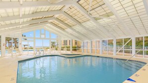 Une piscine intérieure avec des parois en verre transparent, un escalier d’accès et une vue sur l’extérieur.