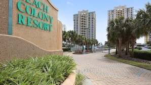 Un panneau indiquant l’entrée du Beach Colony Resort, avec une allée pavée et des palmiers.