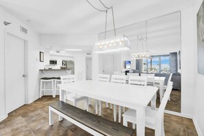 Eine moderne Küche mit weißen Schränken, ein Essbereich mit weißem Tisch und Stühlen sowie ein großes Fenster mit Blick auf die Stadt.