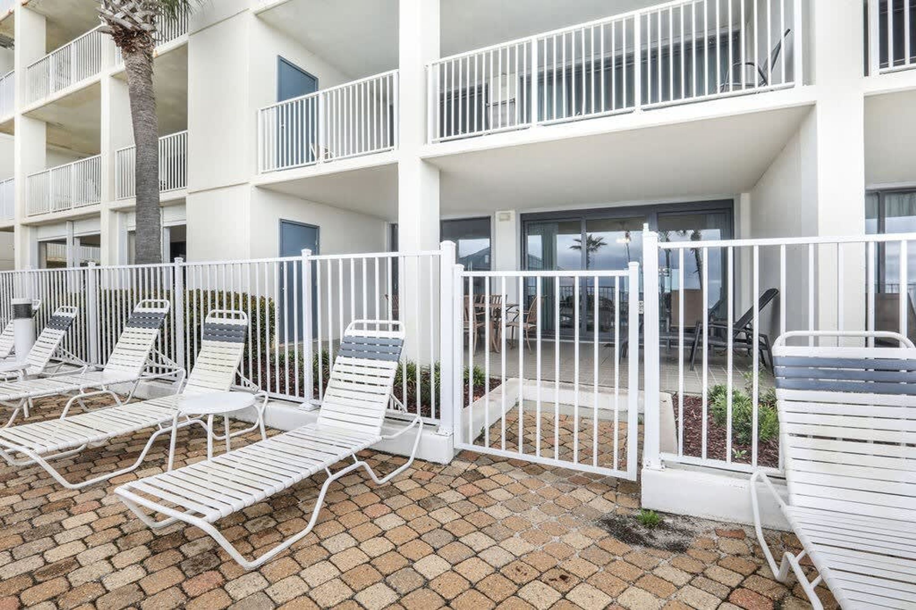 A multi-story building with white balconies and a gated outdoor area with white lounge chairs.