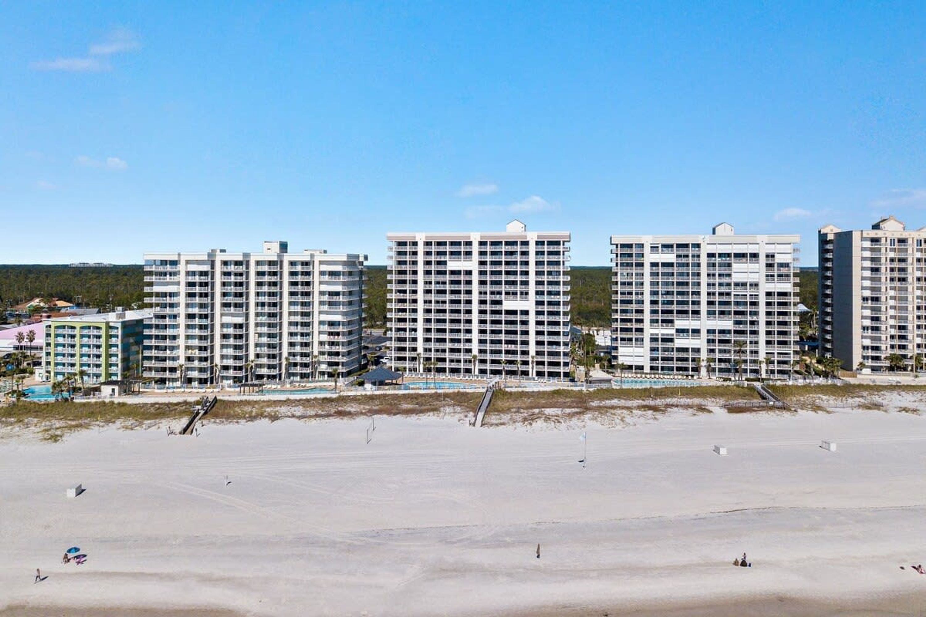 A beachfront hotel with multiple high-rise buildings, a sandy beach, and a clear sky.