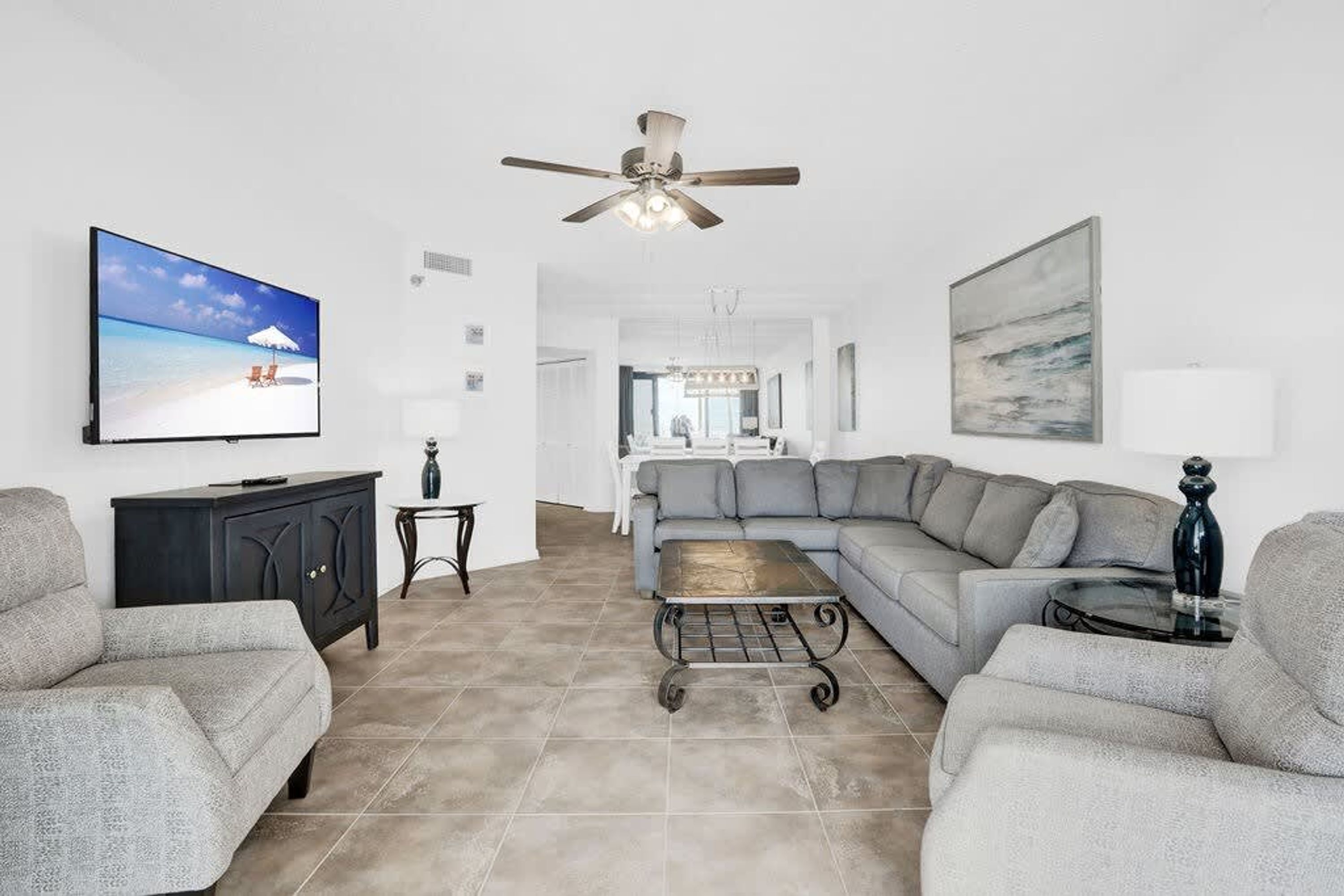 A living room with a sectional sofa, a flat-screen TV, a ceiling fan, and a painting on the wall.