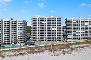Ein Hochhotel mit mehreren Balkonen, einem Poolbereich und Blick auf den Strand.