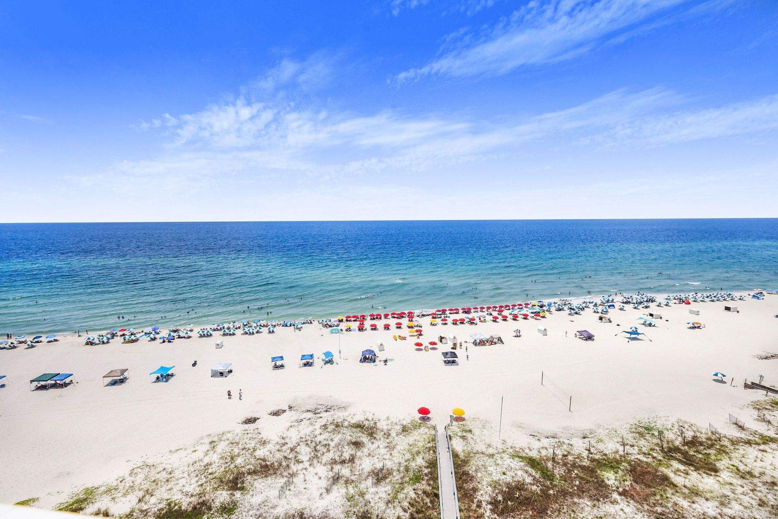 A beach with numerous umbrellas and beach chairs, a clear sky, and calm sea.