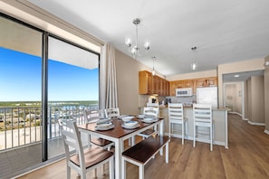 Eine moderne Küche mit Holzausstattung, ein Essbereich mit weißen Stühlen und einem Holztisch sowie ein Balkon mit Blick auf die Stadt.