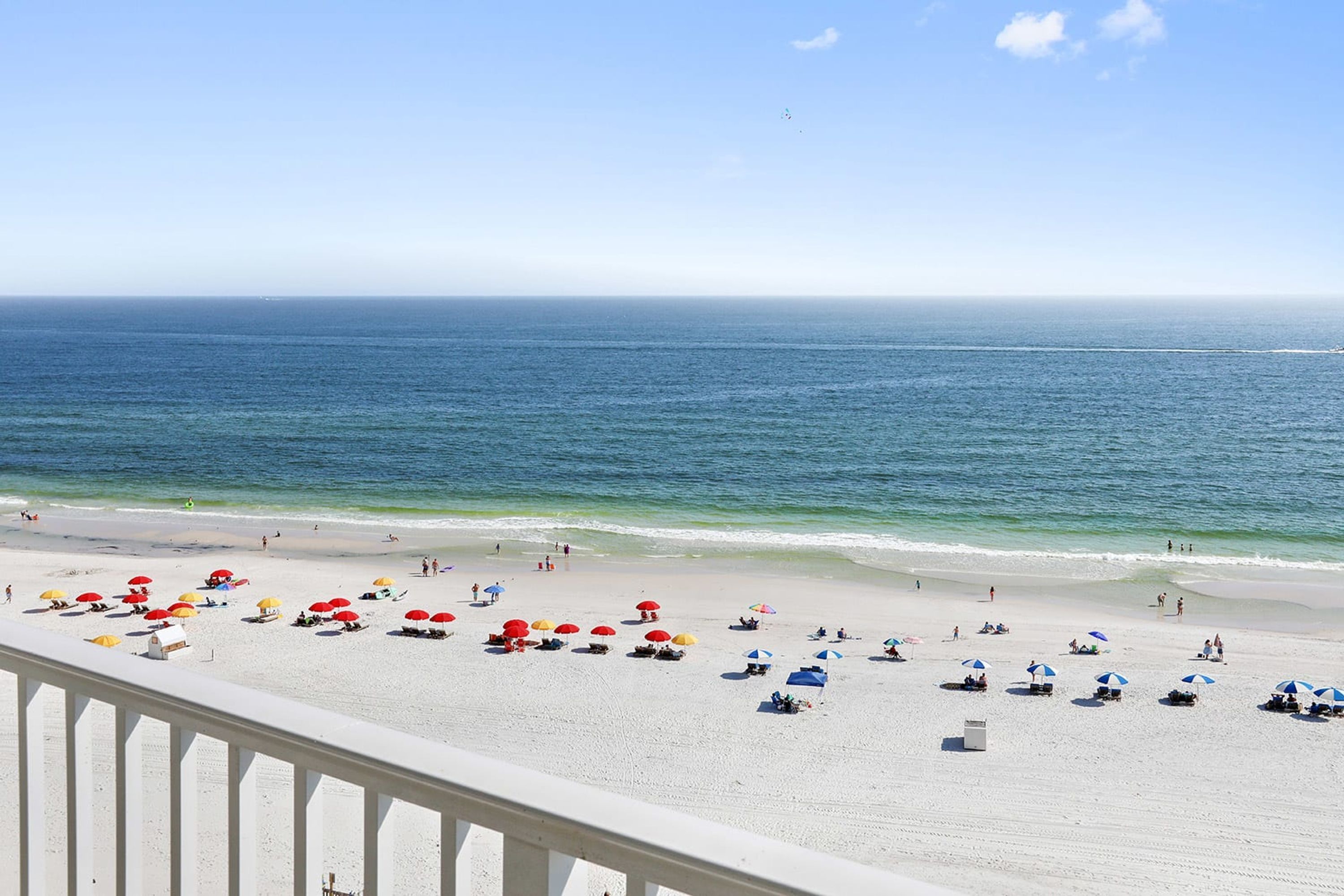 A beach with white sand, clear blue water, and umbrellas.