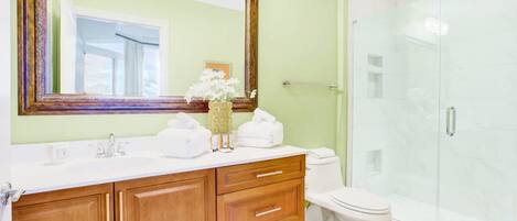 A bathroom with a wooden vanity, a large mirror, a toilet, and a glass shower enclosure.